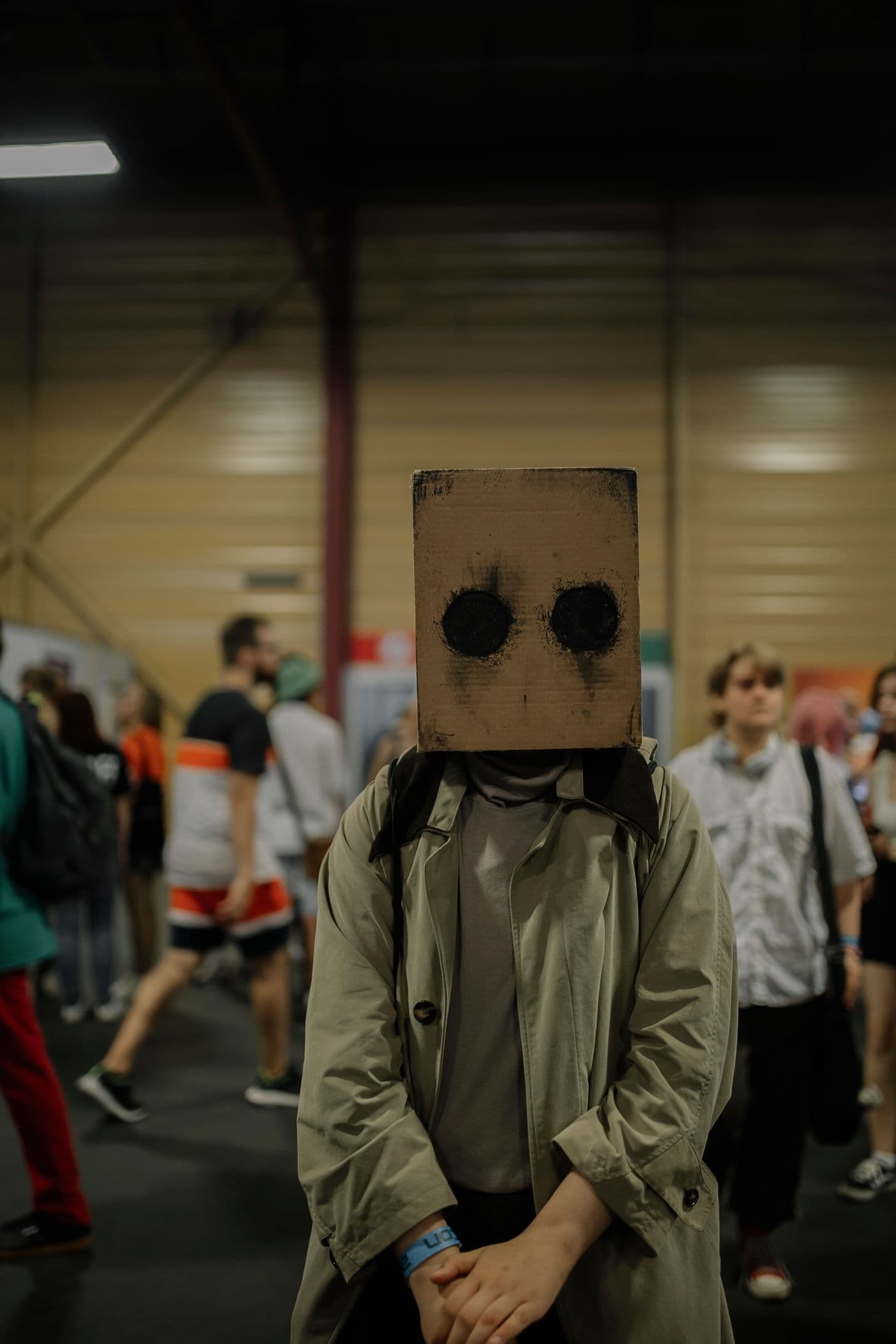 Cosplayer in a handmade cardboard mask and trench coat standing in a convention hall
